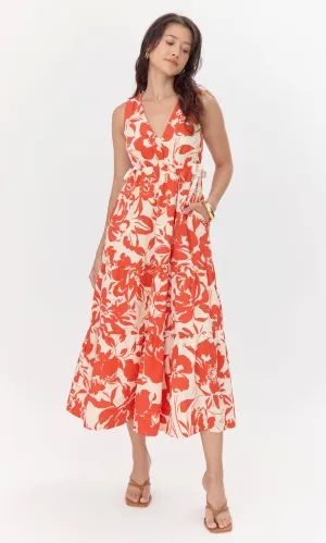 Model wears cream-colored, midi dress with a red, floral pattern. The model puts her hand in 1 of the 2 hidden pockets in the skirt. The dress features a V-neckline and drawstrings on the side of the bodice. 